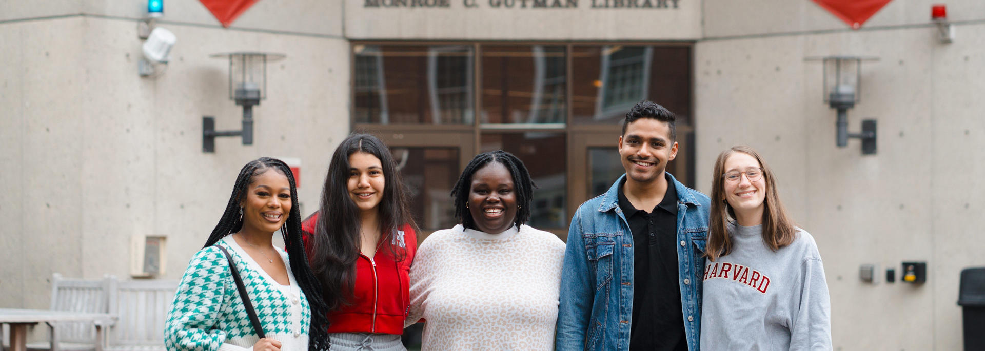 A group of HGSE Community members smile in front of the entrance to Gutman Library.